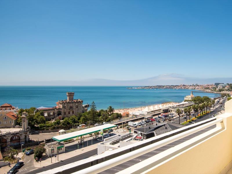 Vista de la costa con playa, mar y edificios junto a la carretera bajo un cielo despejado.