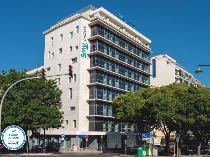 Edificio moderno di un hotel con più piani e grandi finestre, circondato da alberi e cielo sereno.
