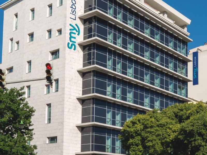 Edificio alberghiero multi-piano con finestre con balcone e albero verde in primo piano.