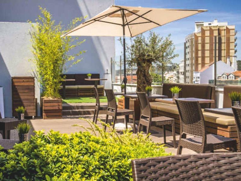 Terrazza soleggiata con diverse aree salotto, piante e un grande ombrellone.