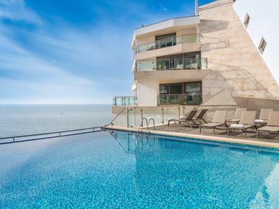 Moderner Außenpool am Gebäude mit Liegestühlen und Blick auf ruhiges, weites Meer unter blauem Himmel.