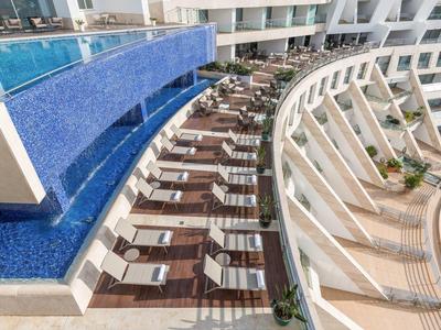 Moderner Poolbereich mit blauer Wasserfläche, Liegestühlen und geschwungener weißer Architektur.