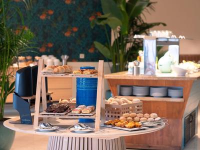 Buffet mit verschiedenen Backwaren und kleinen Snacks auf runden Tellern in modernem Raum.