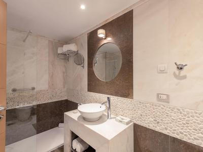 Modernes Badezimmer mit Rundspiegel, Waschbecken auf weißer Ablage und Badewanne mit Duschwand.