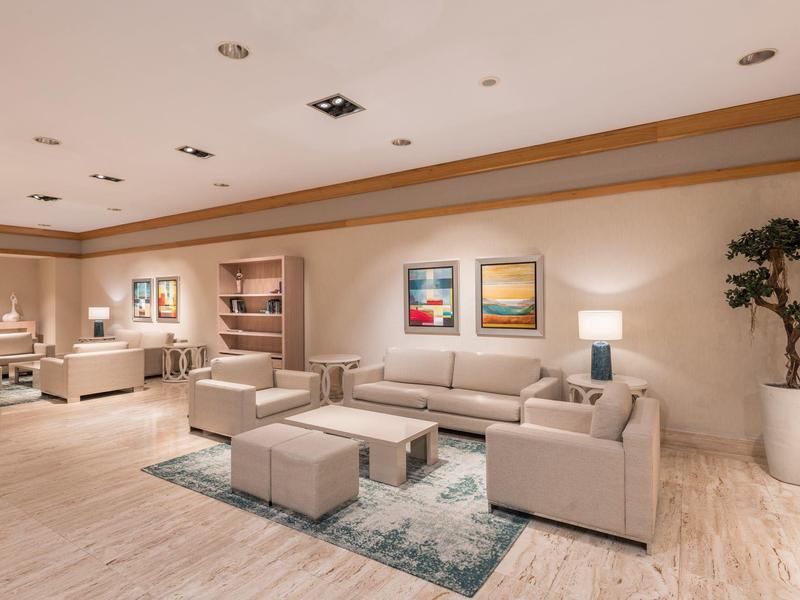 Helles Wohnzimmer mit hellen Sofas, Couchtischen, Teppich, Stehlampe und großer Topfpflanze.