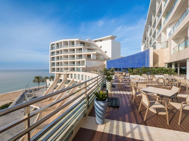 Moderner Balkon mit Holzterrasse, Sitzmöbeln und Meeresblick unter blauem Himmel.