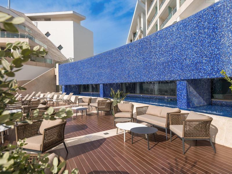 Moderner Außenbereich mit Sitzgruppen, blauem Mosaikwand und Holzboden unter blauem Himmel.