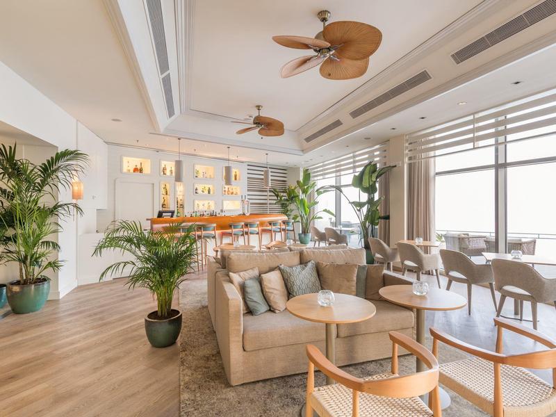 Helles Café mit Holzfußboden, tropischen Pflanzen, Deckenventilatoren und großen Panoramafenstern.