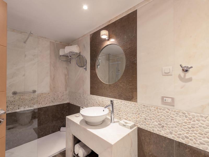 Modernes Badezimmer mit Rundspiegel, Waschbecken auf weißer Ablage und Badewanne mit Duschwand.