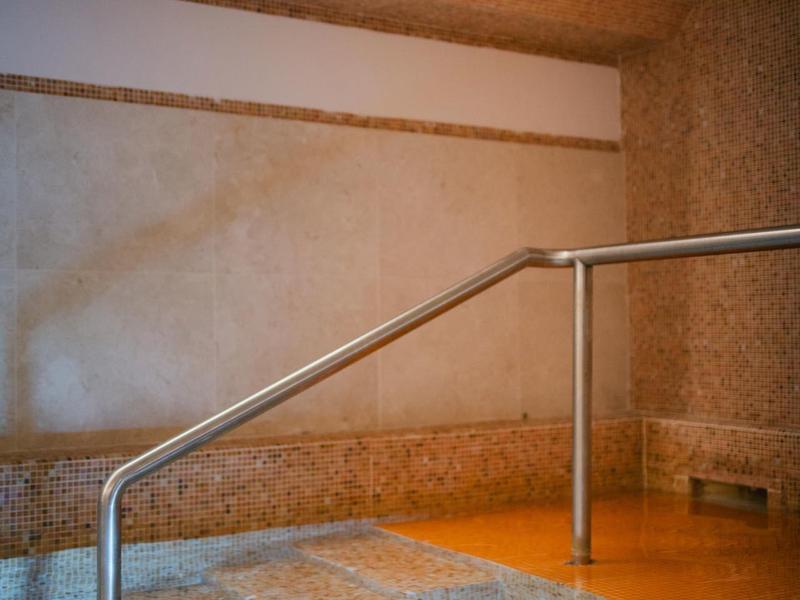 Innenbereich mit Boden aus Steinen, Wasserbecken und Edelstahlgeländer unter hellem Deckenspotlicht.