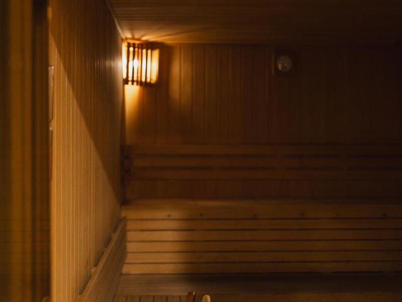 Innenraum einer Sauna mit Holzbänken, Holzwänden und einem beleuchteten Wandlicht.