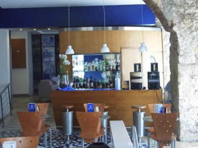 Area bar moderna in hotel con bancone in legno, lampade blu e sedie in primo piano.