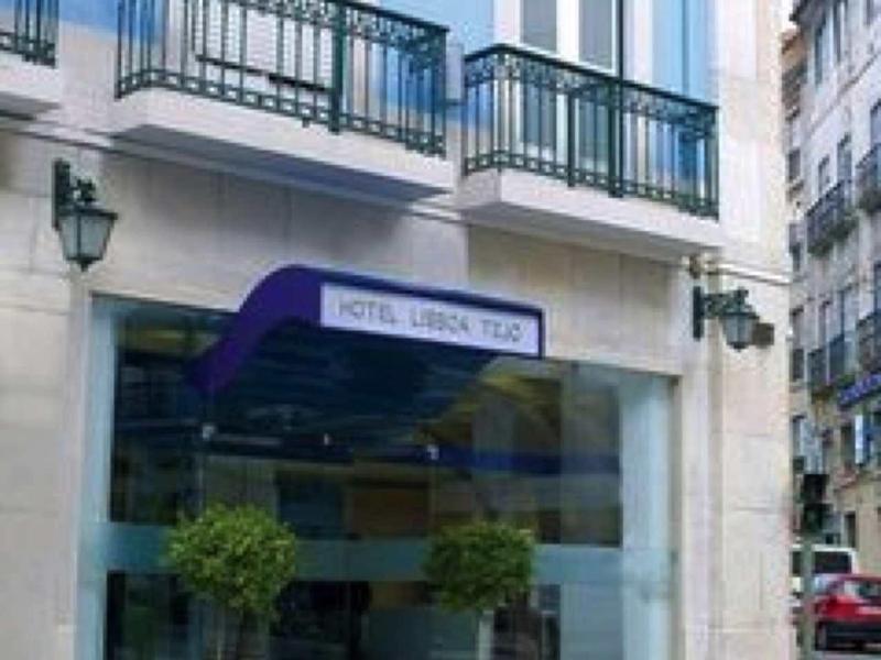 Vista esterna di un hotel con tenda blu e balconi, due vasi di piante blu all'ingresso.