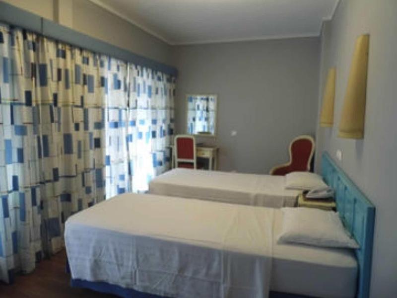 Camera d'hotel con due letti singoli, testiera blu e tende a motivi.