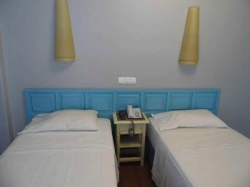 Due letti singoli con lenzuola bianche e testata blu, comodino con telefono tra di loro.