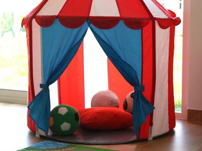 Kolorowy namiot dla dzieci w czerwono-białe paski z dywanem do zabawy z przodu.