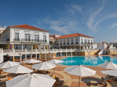 Luksusowy hotel z basenem, leżakami i białymi parasolami pod niebieskim niebem.