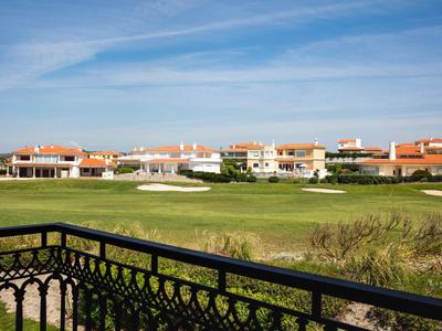 Widok z balkonu na zielone pole golfowe z domami w tle.