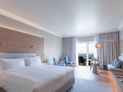 Nowoczesny pokój hotelowy z dużym łóżkiem, miejscem do siedzenia i balkonem z widokiem na morze.