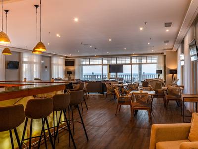 Nowoczesna przestrzeń lounge hotelu z barem, miejscami do siedzenia i dużymi oknami.