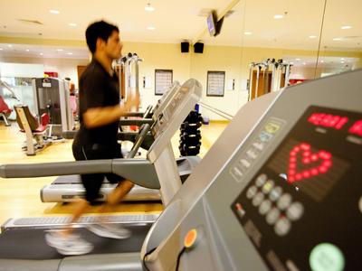 Mężczyzna biegnie na bieżni w jasnej siłowni, na pierwszym planie widoczny monitor tętna.