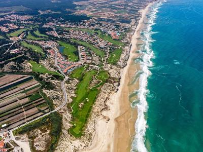 Zdjęcie z lotu ptaka długiego piaszczystego wybrzeża z przylegającym polem golfowym i osadami w tle