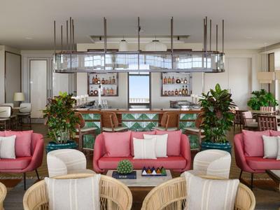 Nowoczesny salon hotelowy z różowymi sofami, drewnianymi krzesłami i barem z roślinami