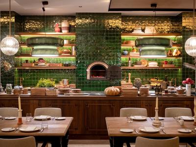 Restauracja z zieloną ścianą z płytek, drewnianym kontuarem i nakrytymi stołami.