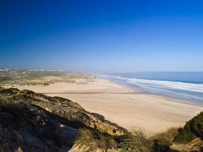 Wieczorny taras hotelowy z miejscami do siedzenia, parasolami i widokiem na morze o zachodzie słońca.