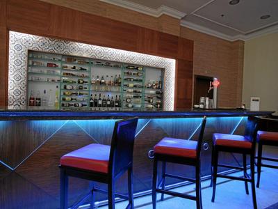 Nowoczesny bar hotelowy z podświetlanym barem i wysokimi stołkami w ciepłej atmosferze.