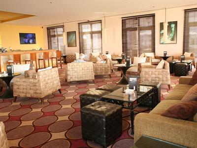 Przytulna hotelowa przestrzeń wypoczynkowa z fotelami, sofami i stolikami na wzorzystym dywanie.