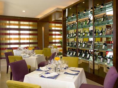 Nowoczesna restauracja z kolorowymi krzesłami, nakrytymi stołami i ścianą z winami.