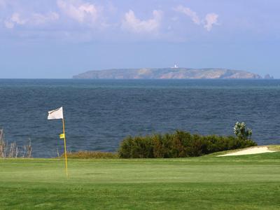 Pole golfowe z flagą na tle morza i wyspy w tle