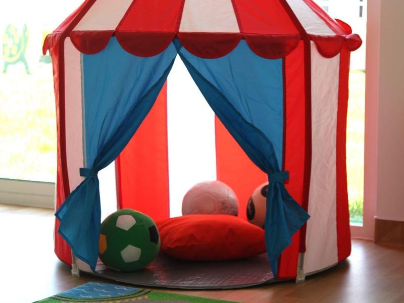 Kolorowy namiot dla dzieci w czerwono-białe paski z dywanem do zabawy z przodu.