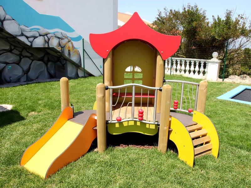 Kolorowy plac zabaw ze zjeżdżalnią na trawniku obok basenu w ogrodzie.