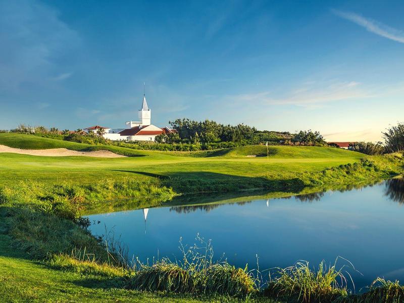 Zielone pole golfowe z oczkiem wodnym i świątynią pod niebieskim niebem o wschodzie słońca