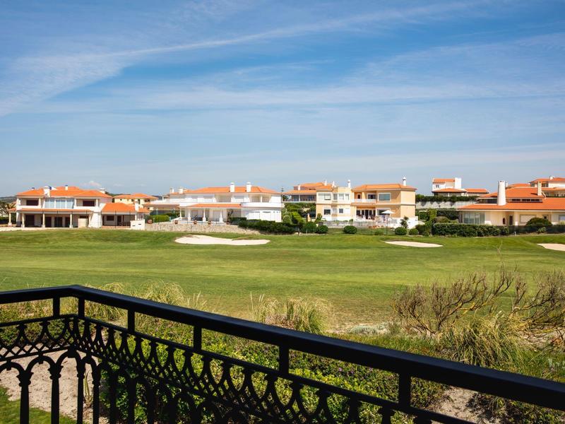 Widok z balkonu na zielone pole golfowe z domami w tle.