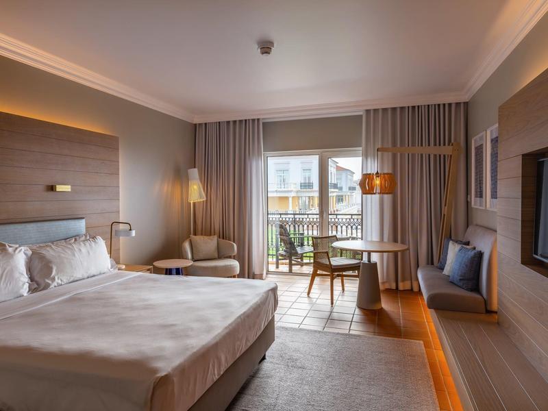 Nowoczesny pokój hotelowy z dużym łóżkiem, miejscem do siedzenia i wyjściem na balkon.