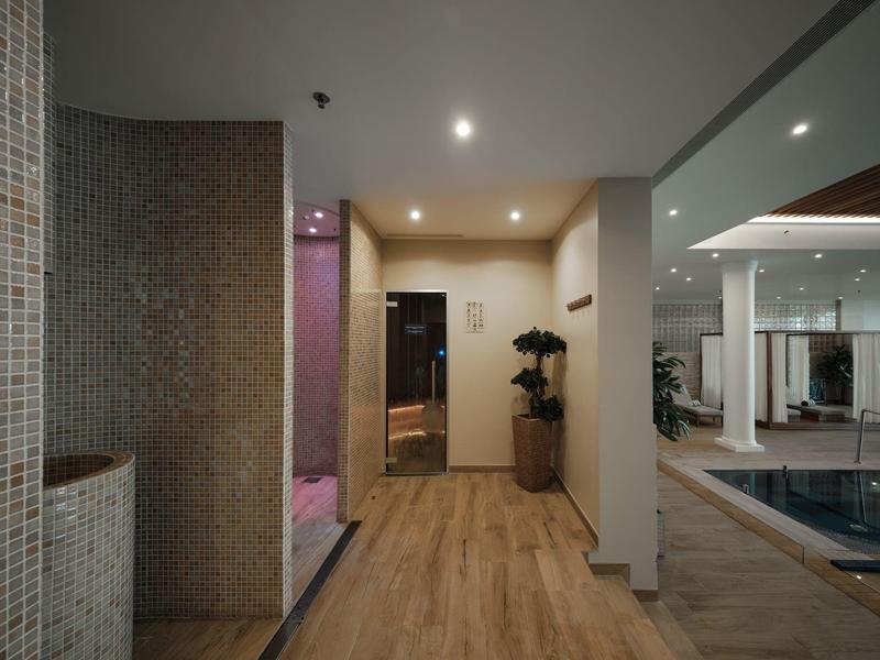 Nowoczesna strefa wellness z drewnianą podłogą, prysznicami i basenem w tle.