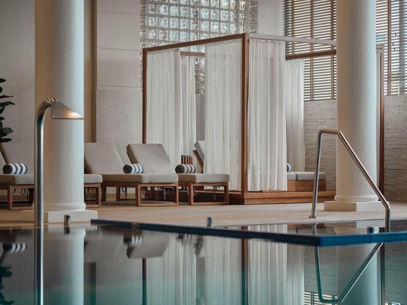 Nowoczesna strefa wellness z basenem, leżakami i zasłonami w jasnym, spokojnym otoczeniu.