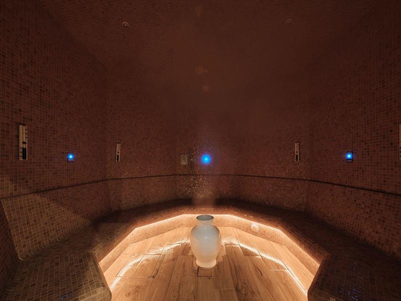 Ciemne pomieszczenie wellness z pośrednim oświetleniem LED i powierzchniami granitowymi.