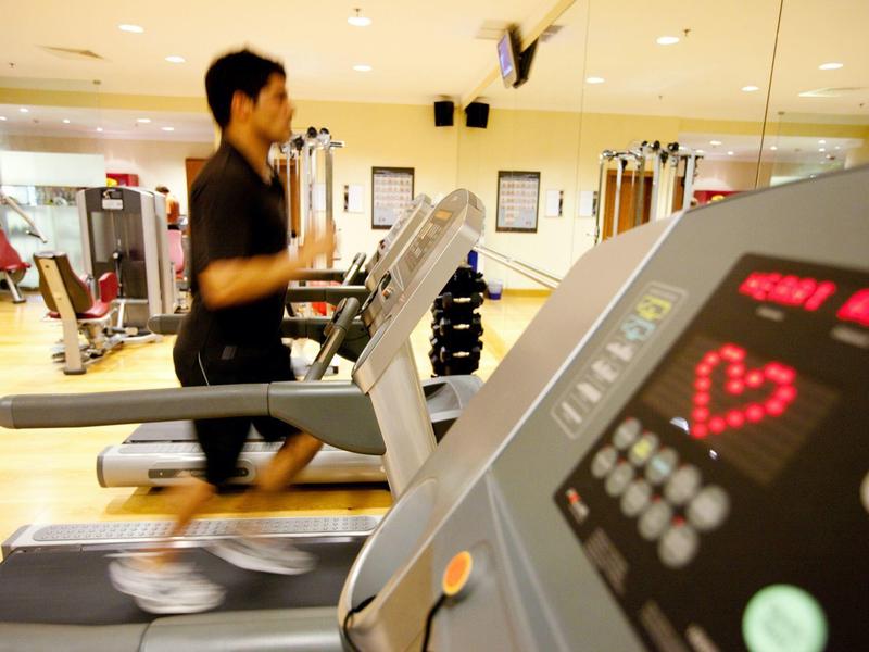 Osoba biegnąca na bieżni w jasnej siłowni z wyświetlaczem tętna na pierwszym planie.