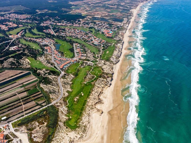 Zdjęcie z lotu ptaka długiego piaszczystego wybrzeża z przylegającym polem golfowym i osadami w tle