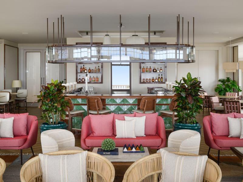 Nowoczesny salon hotelowy z różowymi sofami, drewnianymi krzesłami i barem z roślinami