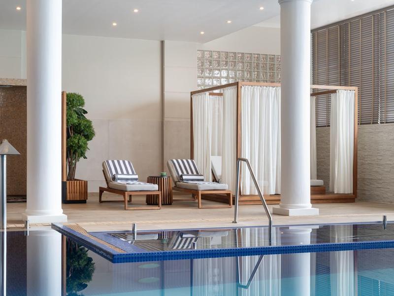 Nowoczesny kryty basen z leżakami i kabinami przebieralni w stylowej strefie wellness.