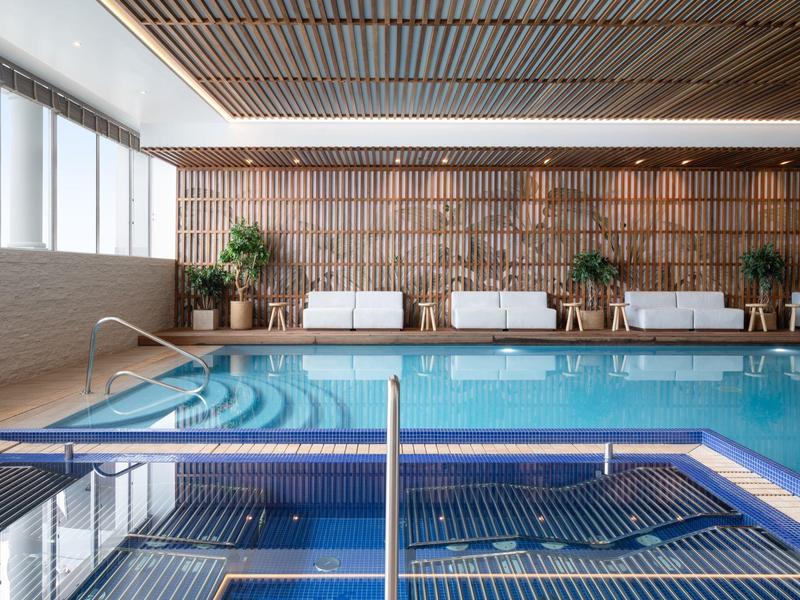 Nowoczesna wewnętrzna strefa basenowa z leżakami i ciepłym oświetleniem.