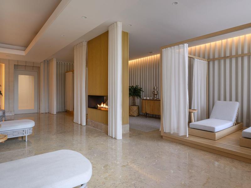 Nowoczesna strefa spa z leżakami, zasłonami i ciepło oświetloną półką.