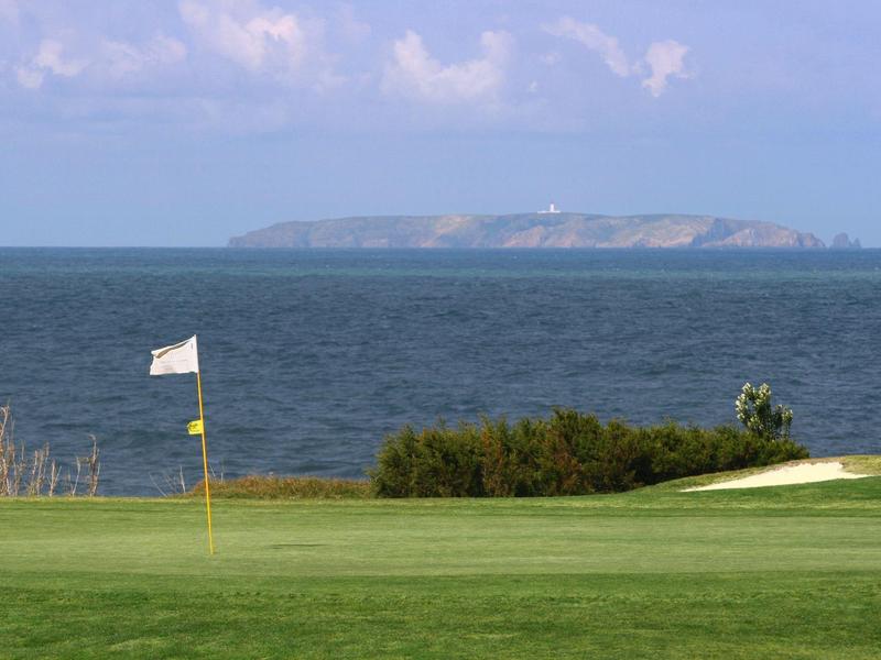 Zielona polana pola golfowego z flagą, morze i wyspa na horyzoncie