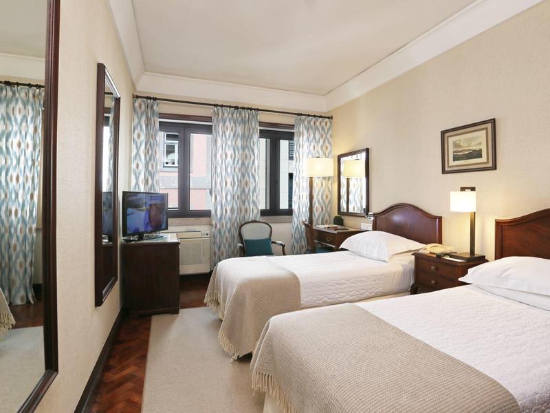 Twin room with wooden furniture, two beds, TV, and large mirror in a neutral design.