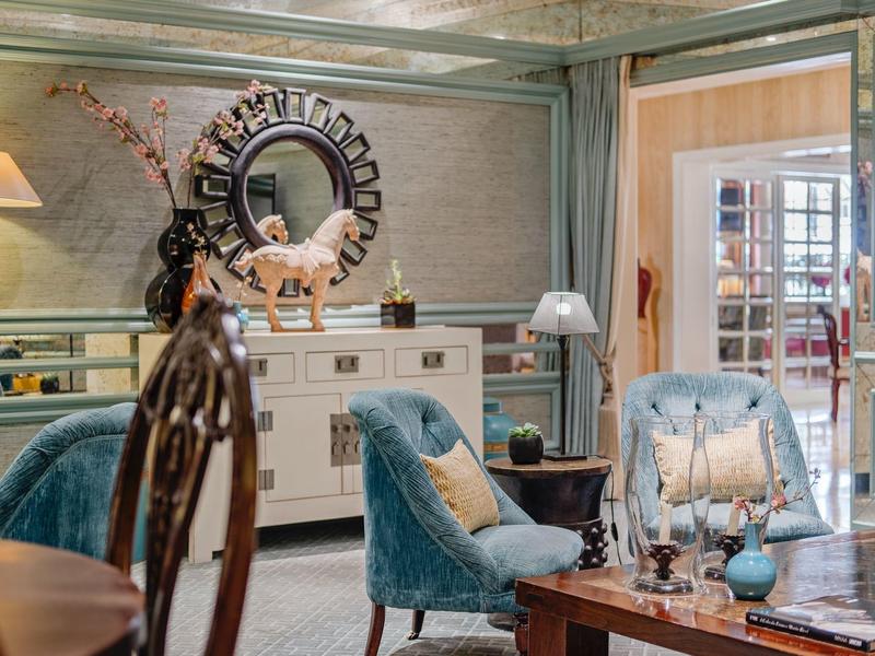 Elegant living room with blue armchairs, mirror above sideboard, and access to a bright room.
